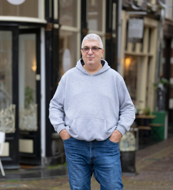 Technisch medewerker poseert in informele kleding in een historische winkelstraat.