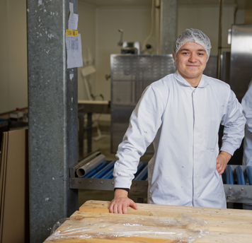 Teamleider productie in witte werkjas en haarnetje bij een productielijn.