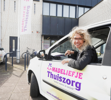 Verpleegkundige van Madeliefje Thuiszorg lacht vanuit de auto voor een zorgbezoek aan huis.