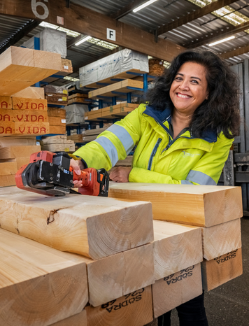 Montagemedewerker in veiligheidskleding zaagt houten balken in een houtopslag.