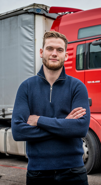 Transportmedewerker poseert voor rode vrachtwagen op bedrijventerrein.