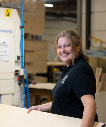 Verkoopmedewerker staat in een werkplaats en glimlacht naar de camera.