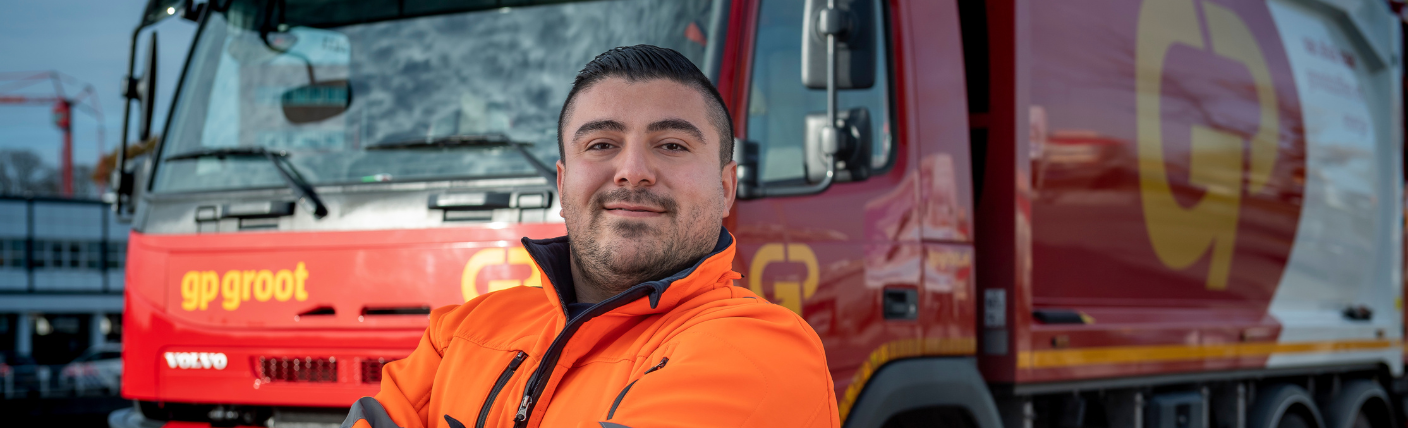 Chauffeur in oranje werkjas poseert voor rode vrachtwagen.