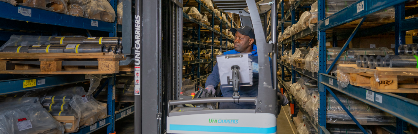 Reachtruckchauffeur aan het werk in magazijn vol metalen onderdelen en rekken.