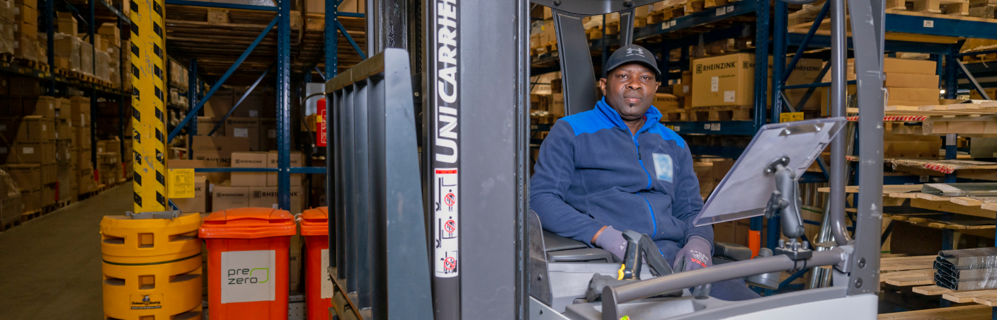 Reachtruckchauffeur in magazijn werkt tussen hoge stellingen met dozen.