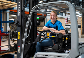 Reachtruckchauffeur glimlacht achter het stuur van een reachtruck in een magazijn.