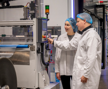 Operators in witte jassen bedienen samen een verpakkingsmachine in een schone productieomgeving