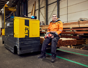 Magazijnmedewerker van Stiho zit lachend op heftruck in houtopslag.