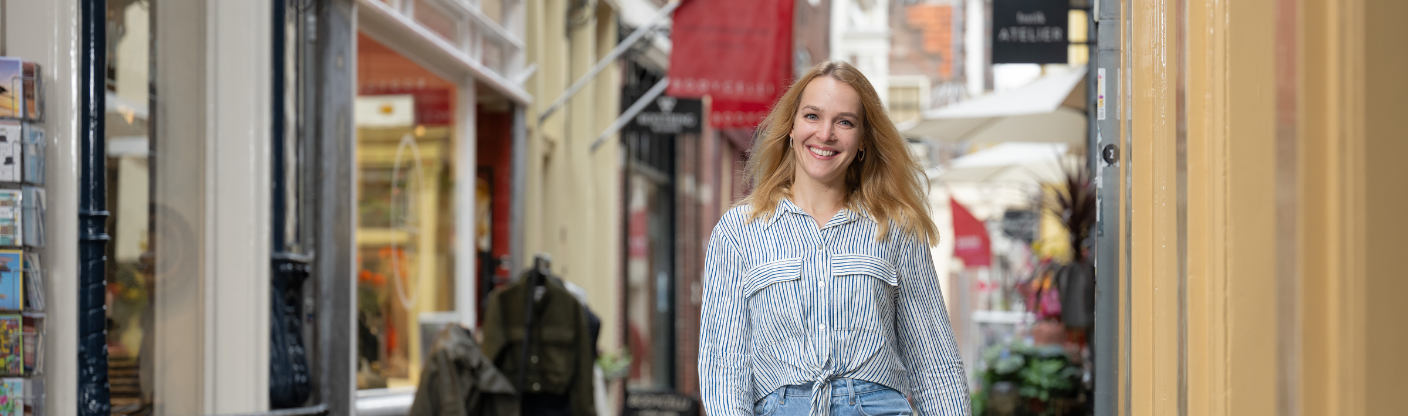 Zorgmedewerker loopt door een winkelstraat met winkels en horecagelegenheden aan weerszijden.
