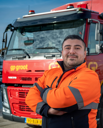Chauffeur in oranje werkjas poseert voor rode vrachtwagen.