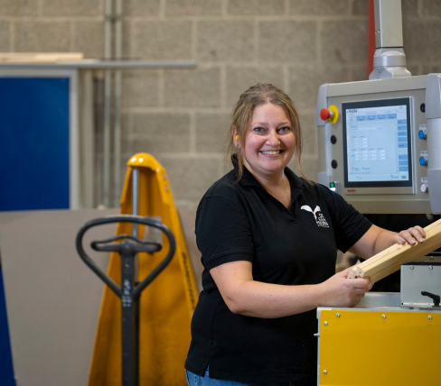 Katarzyna werkt lachend aan een machine in een productieomgeving, blij met haar plek via PDZ