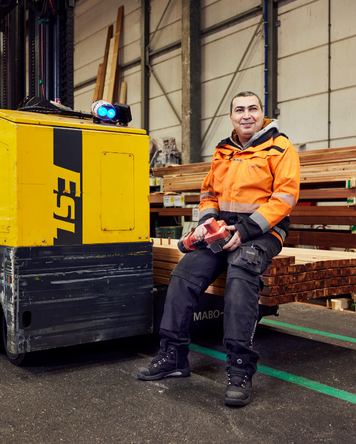 Montagemedewerker in oranje werkkleding zit op een heftruck in een houtmagazijn.