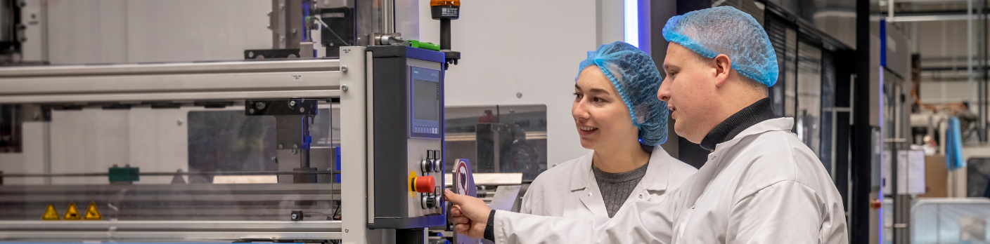 Twee operators in witte jassen en haarnetjes bedienen samen een industriële machine