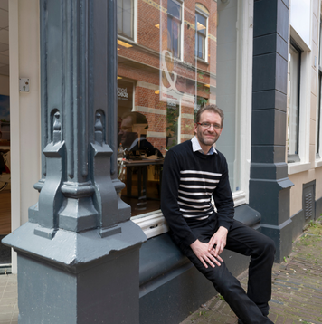 Bijrijder zit ontspannen voor een pand in een historische binnenstad.