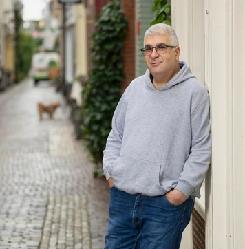 Chauffeur staat ontspannen in een smalle, oude binnenstraat.