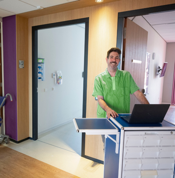 Verpleegkundig werkt met laptop op een medicijnkar in een zorginstelling.