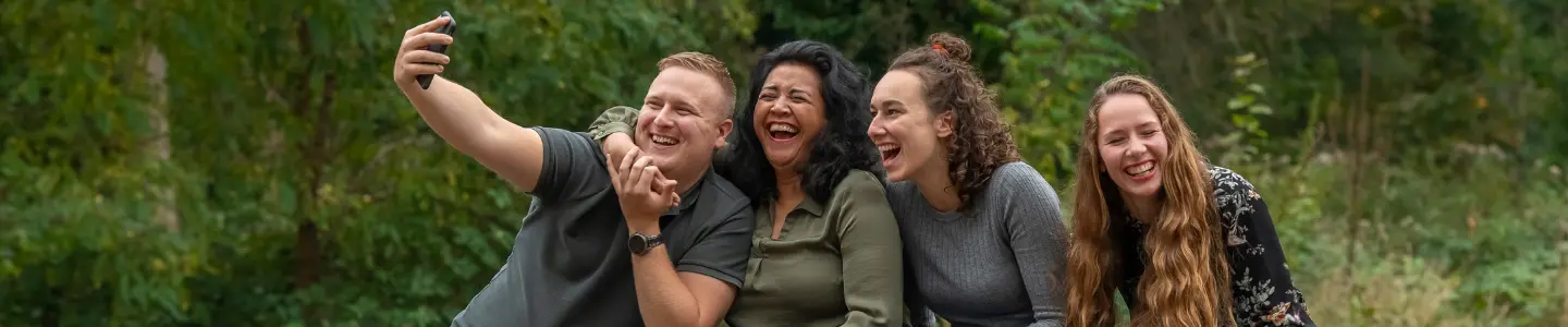 Vier collega’s lachen samen tijdens het maken van een selfie in een bosrijke omgeving.