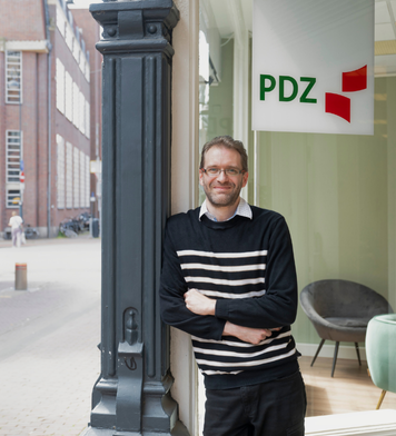 Administratief medewerker staat ontspannen bij kantoorentree.