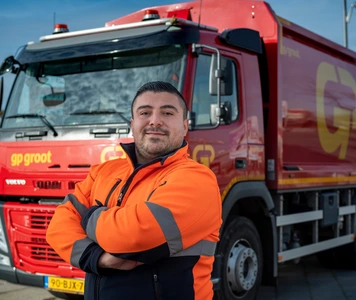 Vrachtwagenchauffeur in werkkleding staat voor een vrachtwagen.