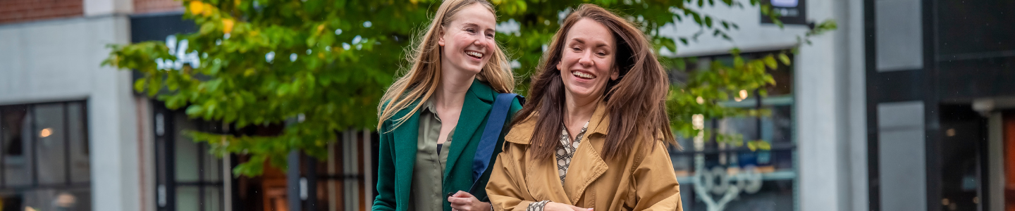 Twee lachende vrouwen wandelen met winkelzakken over een brug in een bruisend stadscentrum