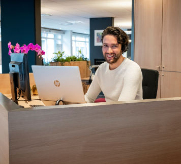 Intercedent met headset lacht achter laptop.