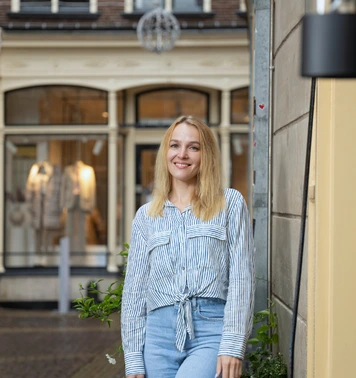 Commercieel medewerker binnendienst staat glimlachend in een winkelstraat.