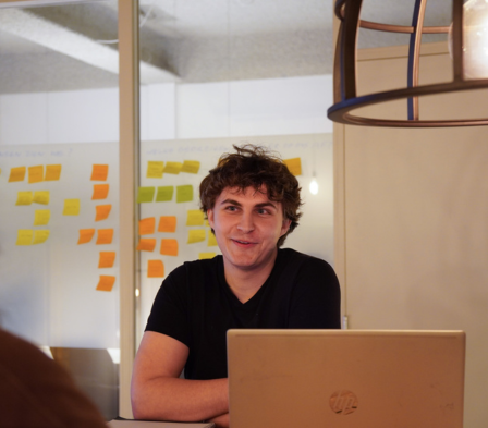 Intercedent zit aan tafel met laptop tijdens overleg op kantoor.