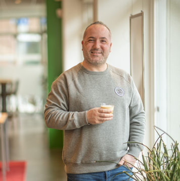 Transportmedewerker met koffie in de hand staat ontspannen bij raam op kantoor.