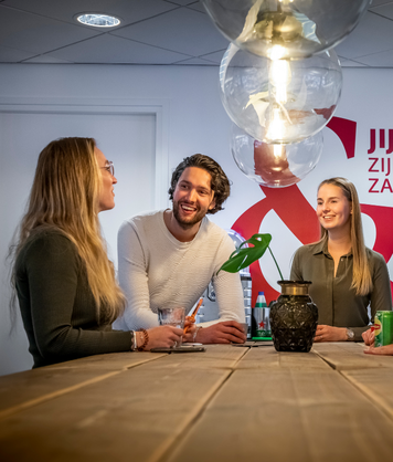 Collega intercedenten staan lachend met elkaar te praten aan een tafel in een moderne kantoorruimte.