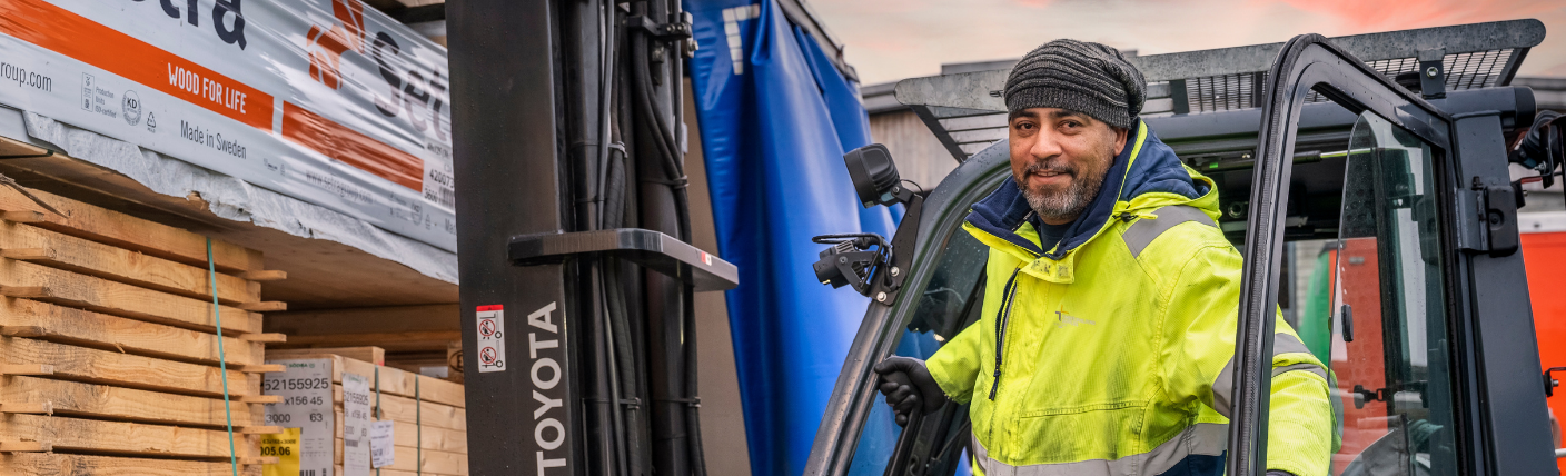 Logistiek medewerker bestuurt heftruck tussen gestapeld hout op buitenterrein.
