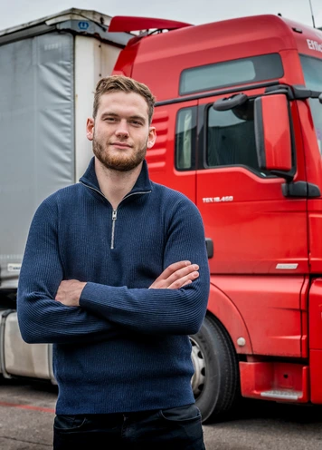 Chauffeur poseert voor rode vrachtwagen op bedrijventerrein.