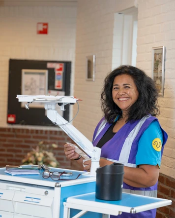 Zorgmedewerker staat bij een verrijdbaar werkstation in een gang van een zorgomgeving.