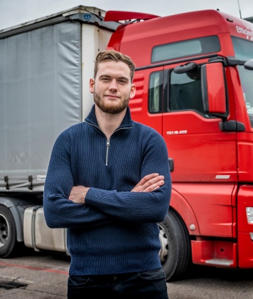 Transportmedewerker poseert voor rode vrachtwagen op bedrijventerrein.