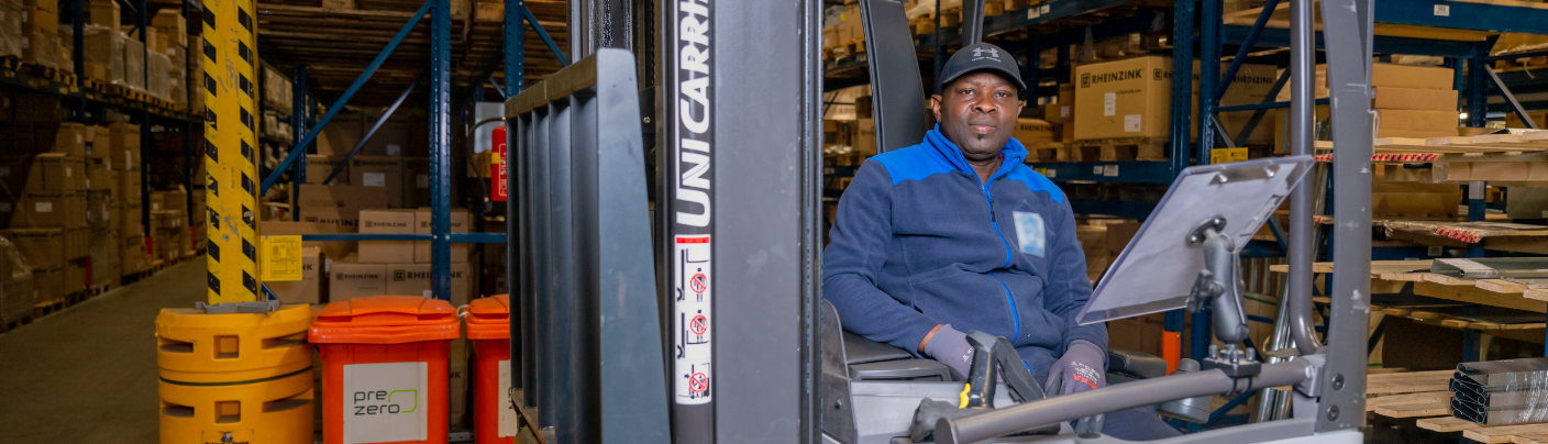 Reachtruckchauffeur in magazijn werkt tussen hoge stellingen met dozen.