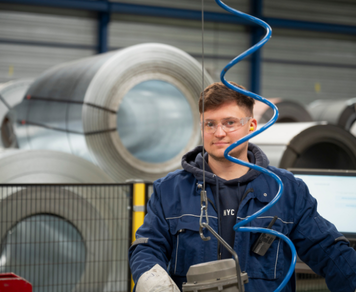 Assemblagemedewerker in blauwe werkkleding en veiligheidsbril werkt met een machine in een fabriekshal.
