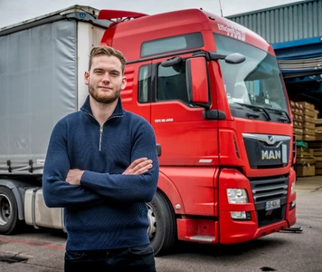 Kandidaat staat met armen over elkaar voor een rode vrachtwagen.