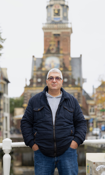 Kandidaat staat op een brug in een stadscentrum met een historisch gebouw op de achtergrond.
