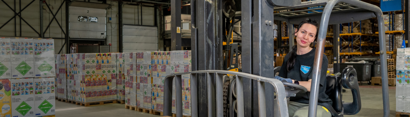 Heftruckchauffeur lacht terwijl ze een heftruck bestuurt in het magazijn.
