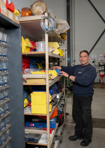 Orderpicker werkt in een magazijn en pakt materialen uit een stelling met verschillende bakken.