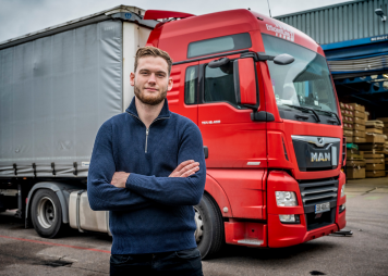 Chauffeur poseert voor rode vrachtwagen op bedrijventerrein.