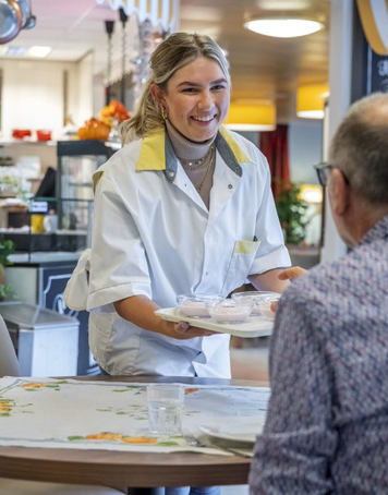 Zorgmedewerker serveert een maaltijd aan een cliënt in de zorginstelling.