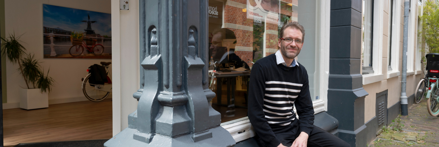 Financieel administratief medewerker zit voor een kantoor en kijkt in de camera.