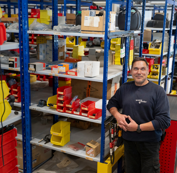 Magazijnmedewerker staat in een magazijn tussen stellingen met onderdelen en bakken.