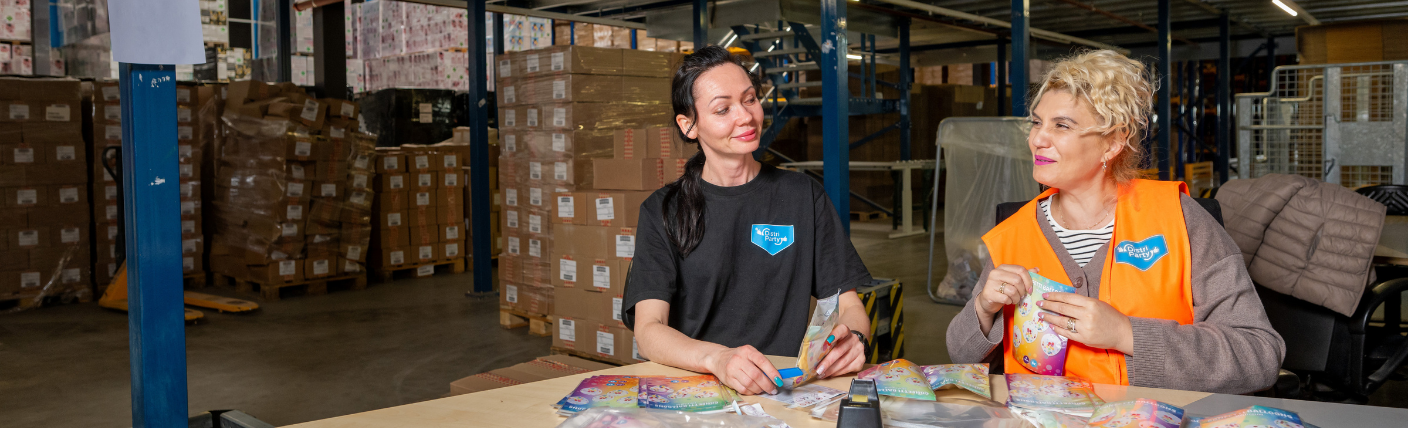 Twee orderpickers verpakken producten aan een tafel in een logistieke omgeving.