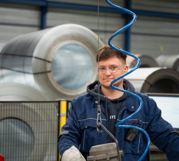 Monteur in blauwe werkkleding en veiligheidsbril werkt met een machine in een fabriekshal.