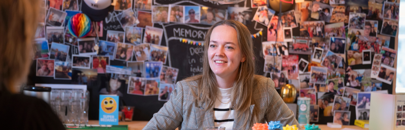 Management assistent in gesprek aan een bureau met foto’s op de achtergrond.