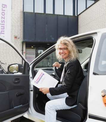 Verpleegkundige stapt met een glimlach uit de auto bij het kantoor van de organisatie.