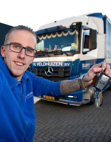 Vrachtwagenchauffeur maakt selfie met sleutels voor zijn blauwe Mercedes-truck.
