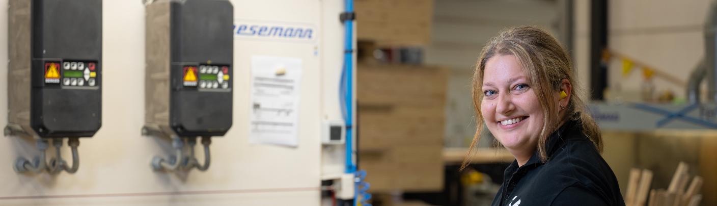 Montagemedewerker glimlacht terwijl zij werkt bij een machine in een industriële werkomgeving.