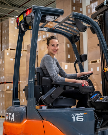 Heftruckchauffeur lacht terwijl ze in een magazijn vol dozen een heftruck bestuurt.